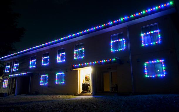 A house illuminated at night with strings of multi-colored Christmas lights around the windows and along the roof.