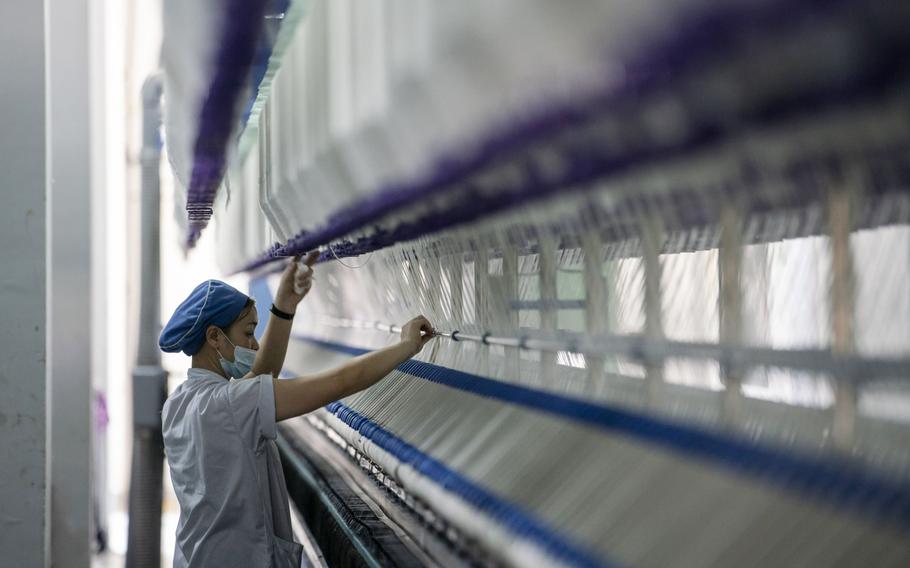 A worker stands in front of a machine on a yarn production line at the Fujian Strait Textile Technology Co. factory in Putian, Fujian province, China, on Monday, Feb. 8, 2021.