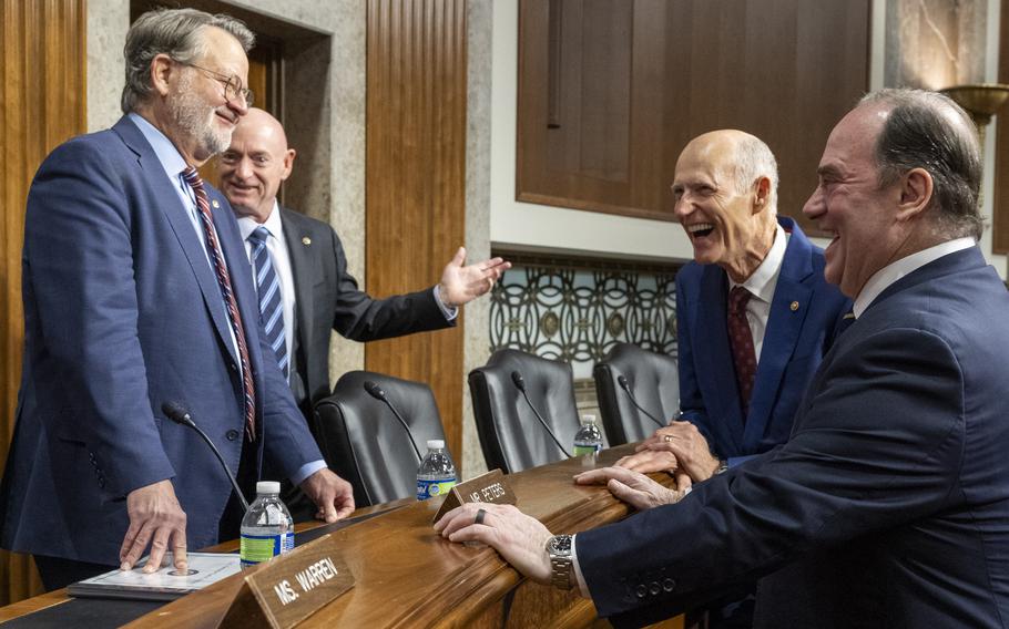 Four men dressed in suits standing in a circle chatting and laughing.