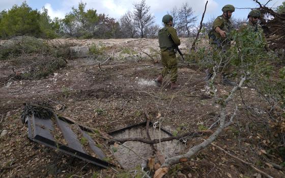 Israeli soldier in fatigues stand among brush next to the entrance to an underground tunnel.