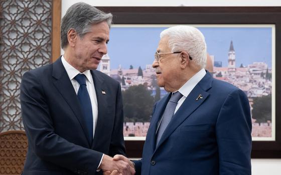 Two men in navy suits shake hands in front of a picture of a city.