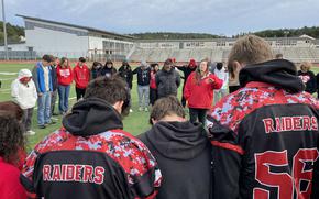 Sarah Ellis leads a prayer for Kaiserslautern High School football player Aiden Wall on Sunday, Sept. 29, 2024, on the schools football field. Hall is in critical but stable condition after suffering a medical emergency on Friday in a junior varsity football game against Stuttgart. Hundreds of community members turned out for the vigil Sunday, including parents of fellow football players, such as Ellis.