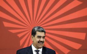 Nicolas Maduro smiles in front of a red wall or poster.