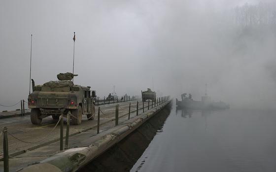 Shielded from view by smoke created by smoke track vehicles of the 4th Chemical Company, military vehicles cross the Imjin River.