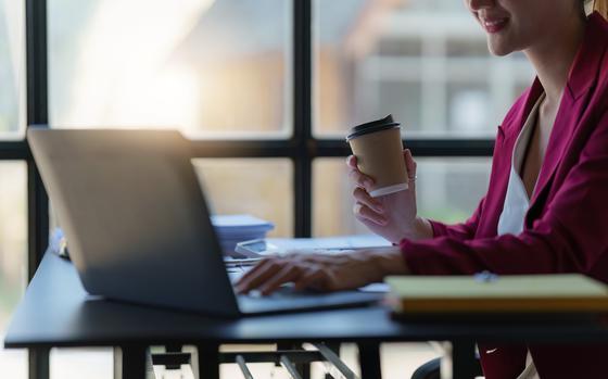 Businesswoman holding coffee cup and working on laptop in office