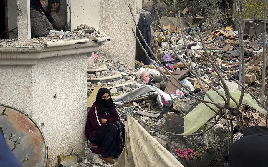 Three women gather together among the rubble of a destroyed building.