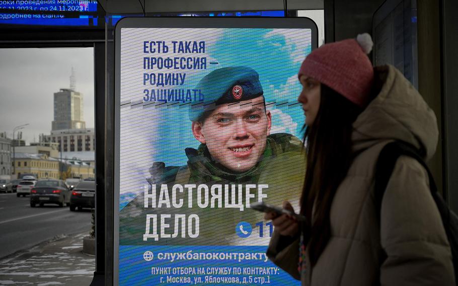 A woman waits at a bus stop with an advertising screen promoting contract military service in the Russian army and reading “There is such a profession to defend fatherland,” in Moscow on Nov. 22, 2023. 