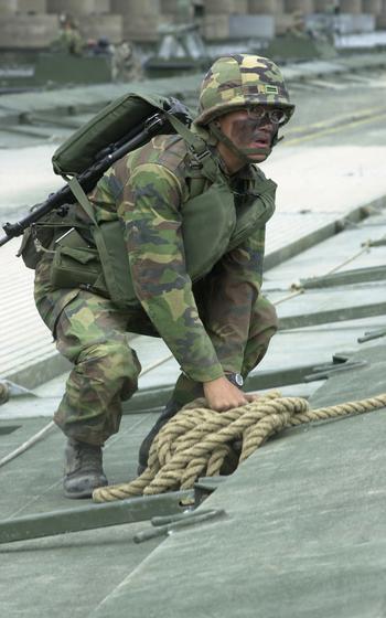 A soldier crouches while they handle rope.