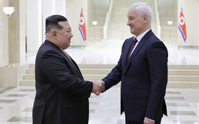 North Korean leader Kim Jong Un and Russian Defense Minister Andrei Belousov, both wearing dark suits, shake hands in the marbled lobby of a government building.