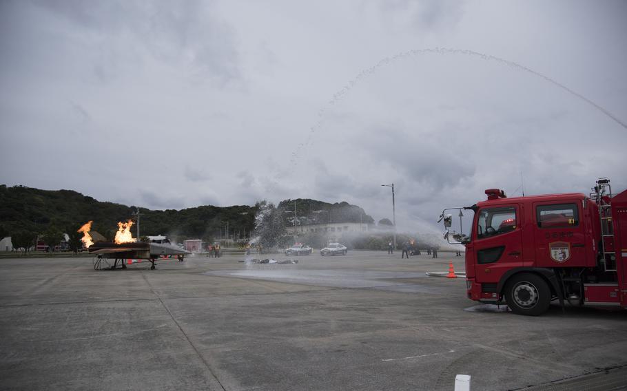 Uruma city firefighters in a red firetruck shoot water at a mock aircraft engulfed in flames.