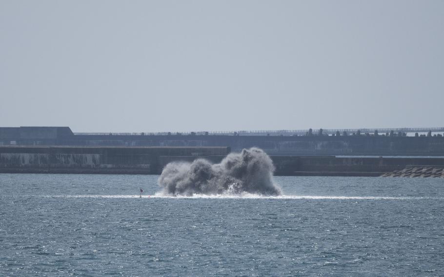 A cloud of smoke and water rise from the water after Japanese divers detonate shells.