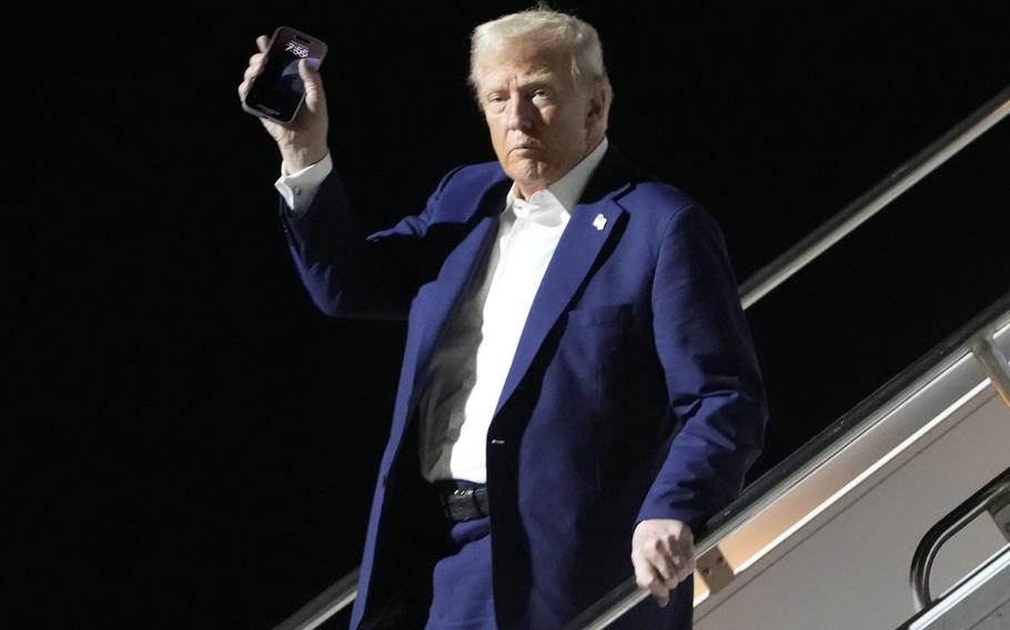 President Trump raises a hand with a phone while descending from Air Force One.