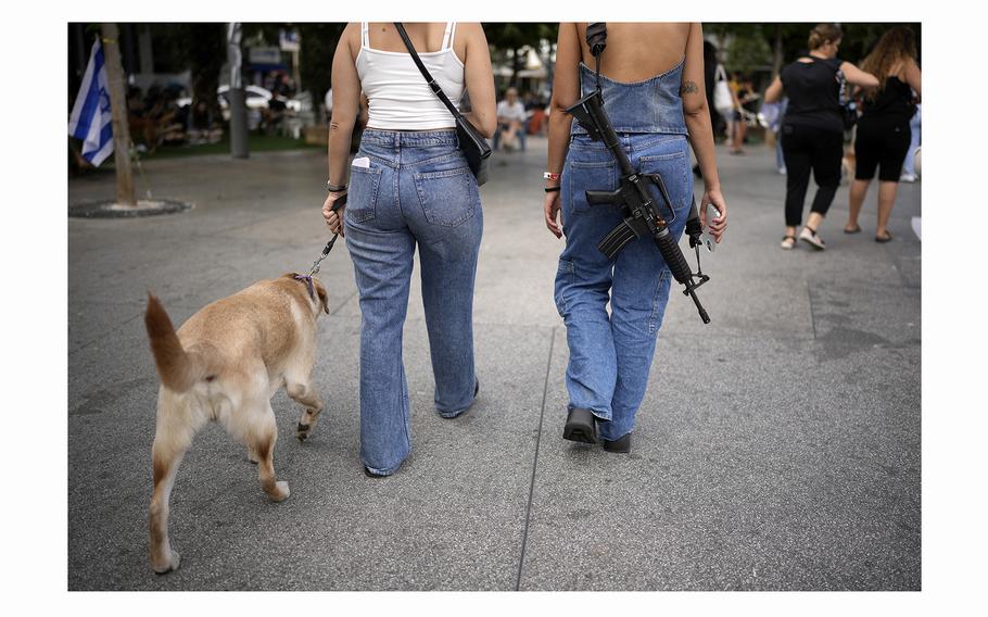 A woman carries an assault rifle as she and a friend walk a dog in Tel Aviv, Israel, on Nov. 11, 2023, a month after Hamas's Oct. 7 attacks.