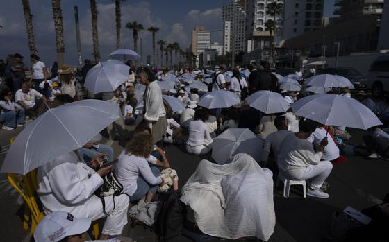 Protesters wearing white clothes and white umbrellas sit on a street.