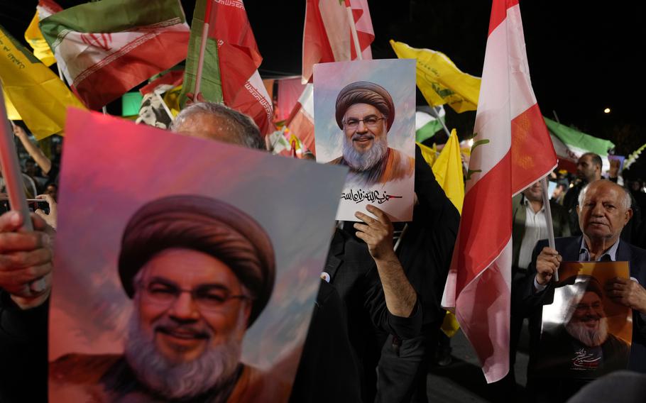 People hold up pictures of Hasan Nasrallah with multiple flags in the background.