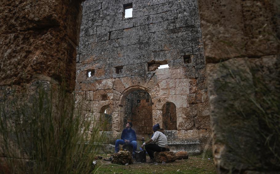 Two young men smoking a hookah while sitting inside an ancient structure in the Dead Cities archaeological site.