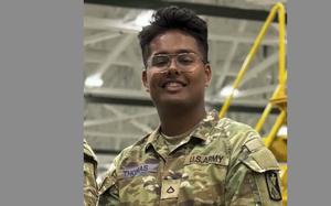 A man in an Army uniform and wearing glasses smiles.