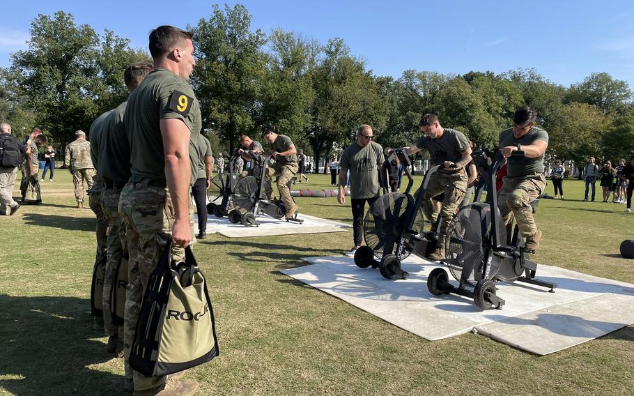 Three soldiers hold weighted bags while two of their counterparts use exercise bikes in front of them during the Army Best Squad Fitness Event in Washington, D.C., Oct. 12, 2024.