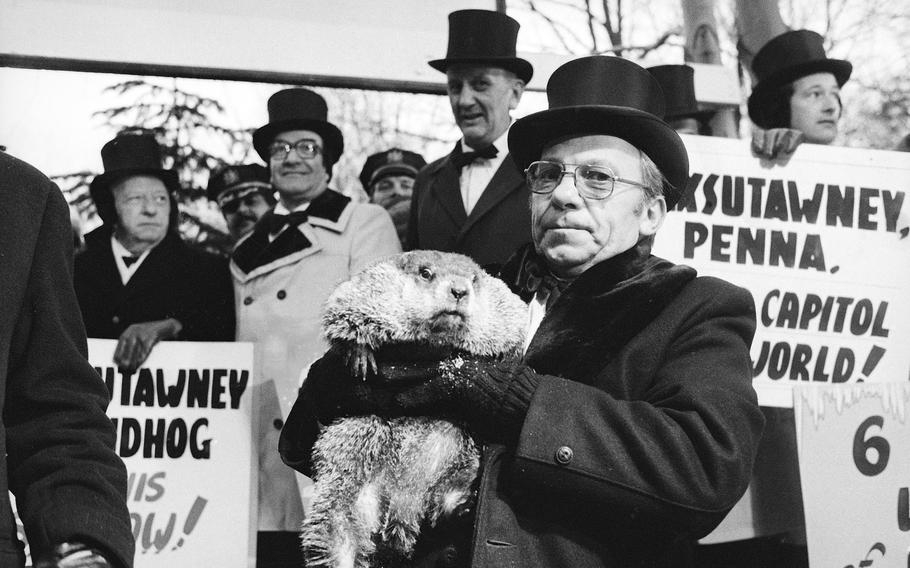 Jim Means, wearing a top hat, holds up Punxsutawney Phil.