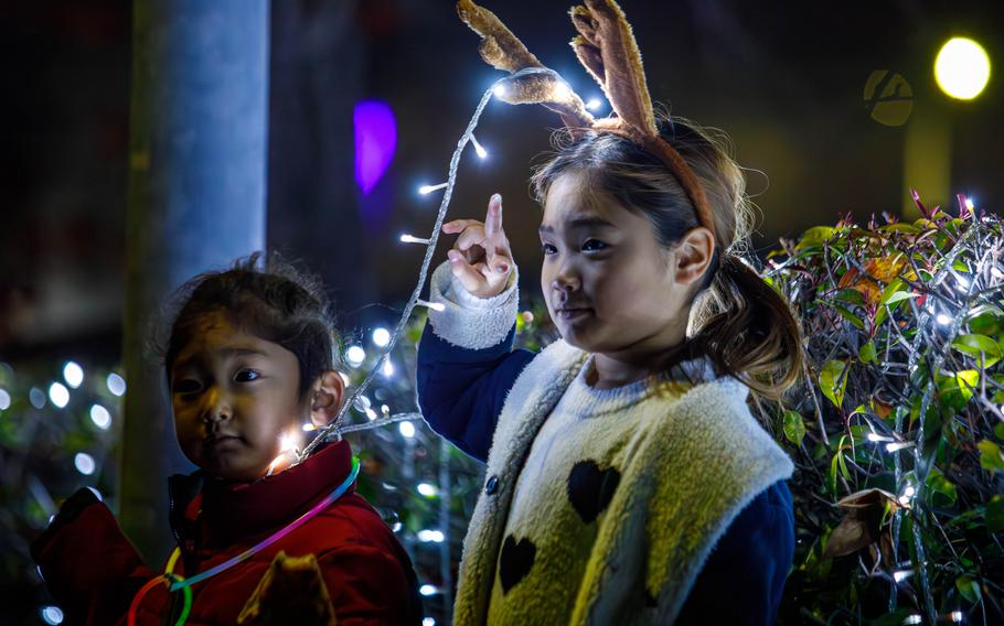 A young girl wearing reindeer antlers with lights strung between them and a young boy enjoy the tree lighting ceremony.