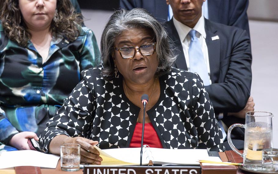 A woman in a black and white sweater sits in front of a microphone with a desk sign that says United States.