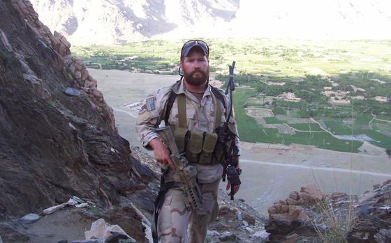 A man on a stony hill in uniform with a rifle in one hand.