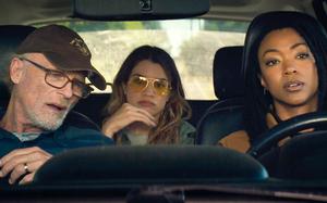 An older man and a young woman in the front seat of a car, seen from the dashboard, with a second woman in the back seat.