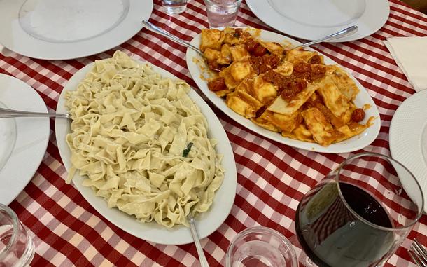 Tagliatelle and ravioli noodles rest on a table covered with a red-and-white-checkered tablecloth.