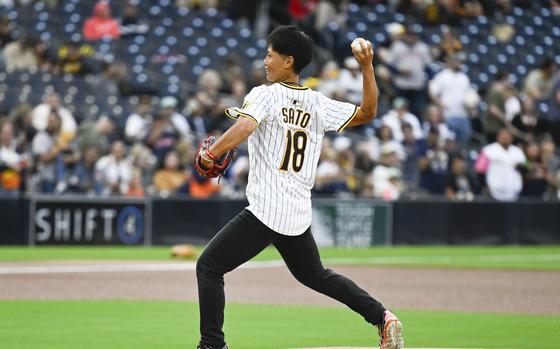 A woman in a professional baseball jersey throws a baseball on a baseball diamond.