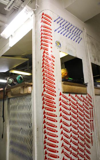 The maintenance desks of aircraft squadrons aboard the USS Dwight D. Eisenhower were lined with victory marks akin to those affixed to their aircraft. At the maintenance desk for Strike Fighter Squadron 131 “Wildcats,” red and blue stencils of bombs and missiles representing successful combat engagements covered the wall from ceiling to floor. 