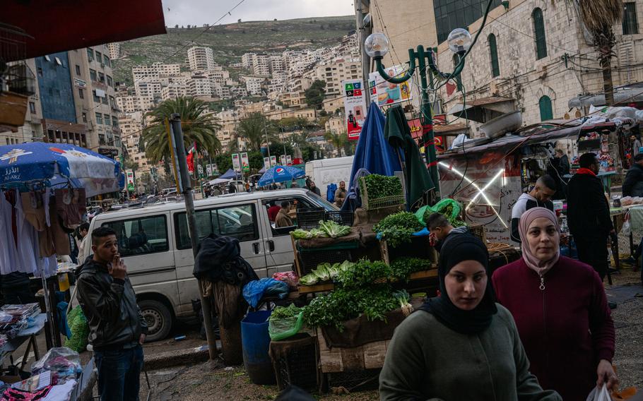 People walk by vendors and shops in a busy traffic circle in central Nablus in the West Bank on March 7, 2024.