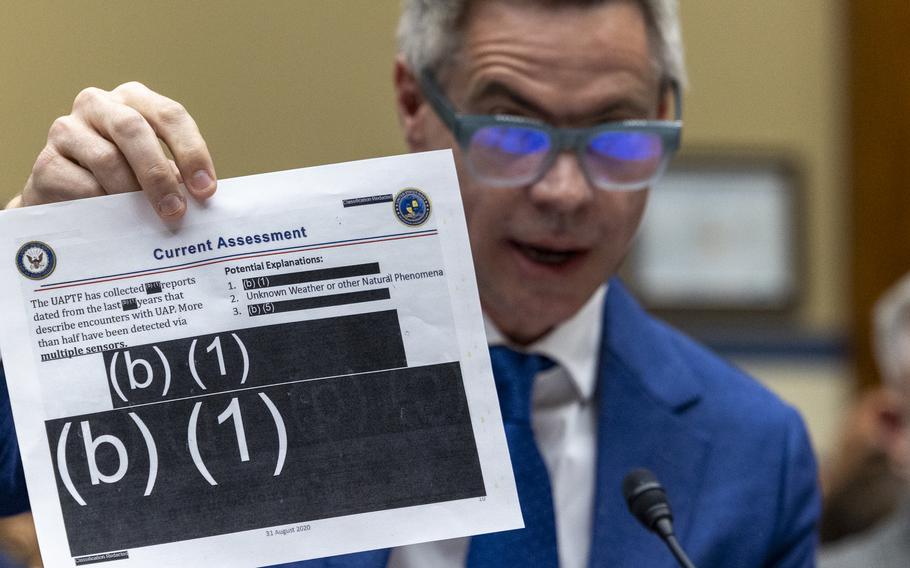 Michael Shellenberger holds up a document that says “Current Assessment” at the top and  is mostly blocked off by black redactions.