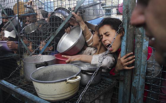 Children shout as they hold out bowls through a gate.