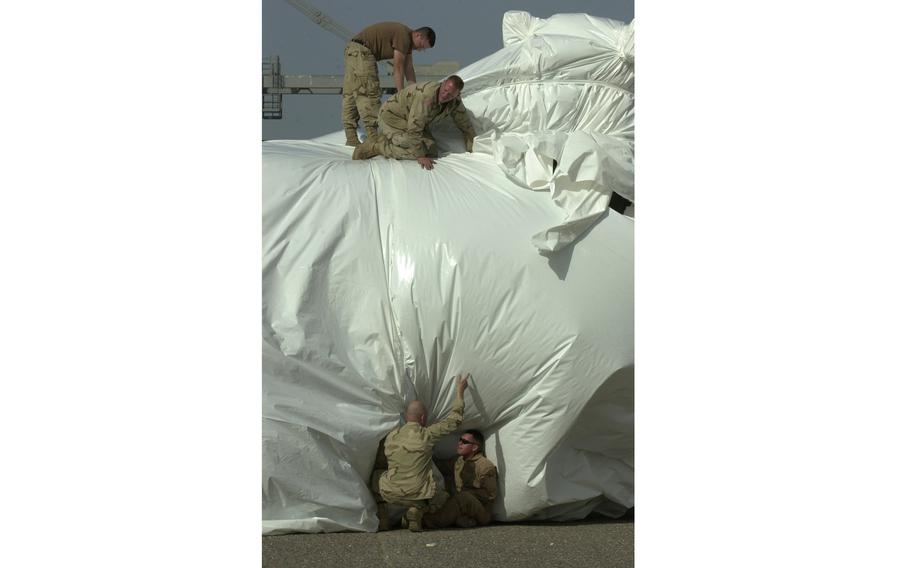 Soldiers wrap plastic around a Chinook helicopter