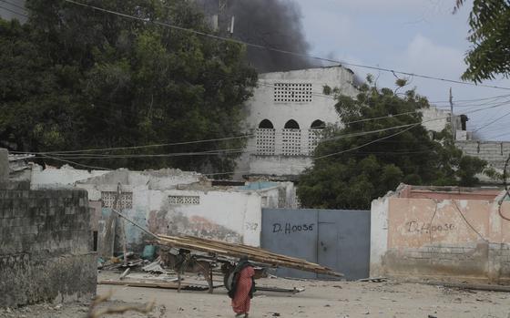 A woman walks on the beach as black smoke is seen rising in the background following an attack in Mogadishu, Somalia, Saturday Aug. 3, 2024. Police in Somalia said Saturday that 32 people died and 63 others were wounded in an attack on a beach hotel in the capital, Mogadishu, the previous evening. (AP Photo/Farah Abdi Warsameh)