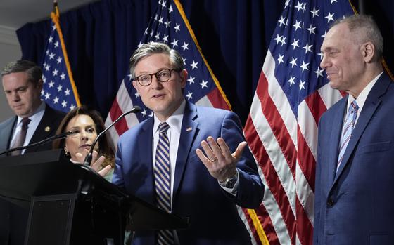 Three men and one woman by a podium in front of three American flags.