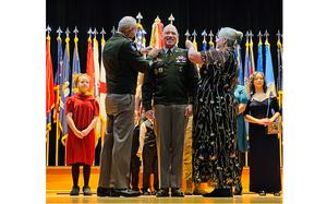 An Army general in the center, with a man and woman adjusting his uniform and pins on either side of him.