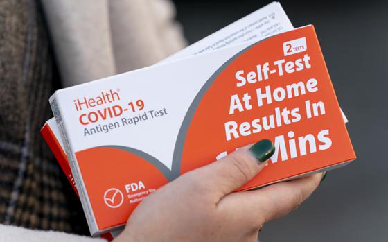 FILE - A woman holds two boxes of at-home Covid-19 test kits in Washington, Dec. 22, 2021. (AP Photo/Andrew Harnik, File)