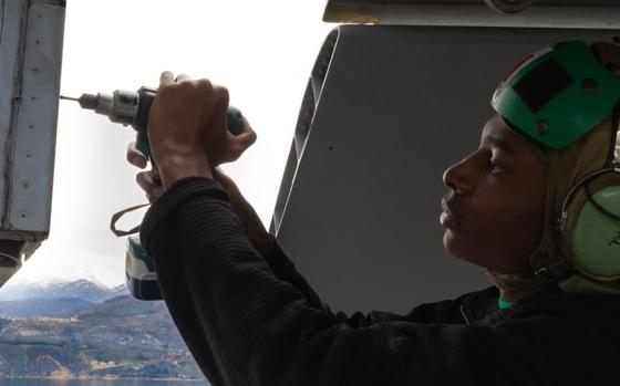 A sailor holding a drill repairs the USS Harry S. Truman.