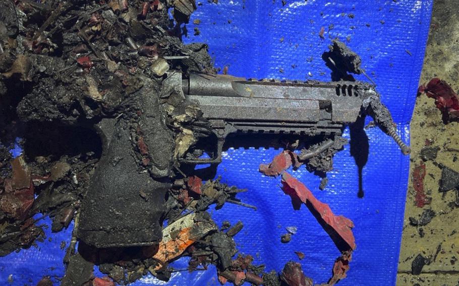 A handgun charred from an explosion sits among debris on a blue tarp.