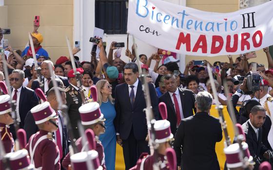 Nicolas Maduro and Cilia Flores arrive in the center of the photo, surrounded by men in black suits, what looks like an honor guard and people smiling and taking pictures.