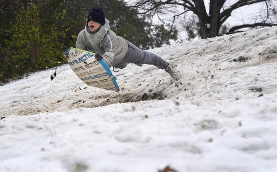 A boy swings off from the snow on a sled that he is holding under his stomach.