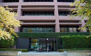 Exterior view of the front of a government office building, with greenery around the entrance.