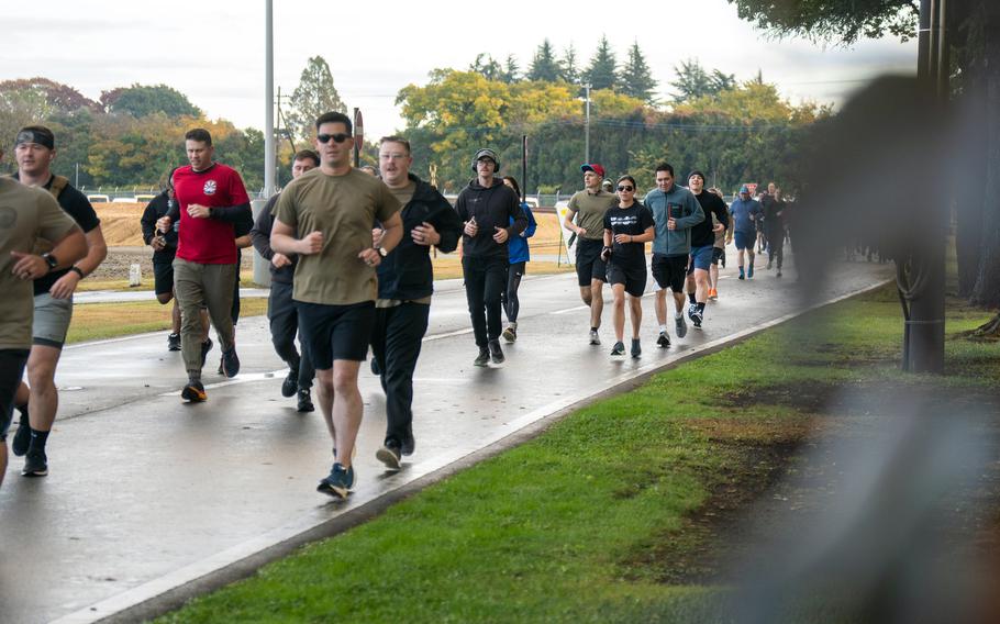 Participants in running attire run on a paved road next to a patch of grass during a 5K race.