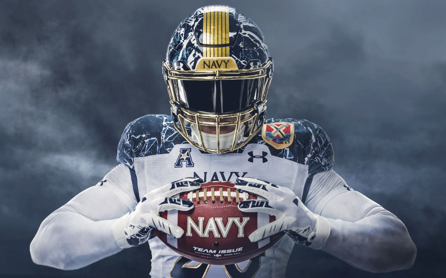 A Navy football player holds a football that says Navy. He is wearing a uniform with a white jersey and a blue and white marble helmet.