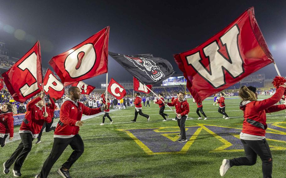 People in red carrying red flags run in a circle on a football field.