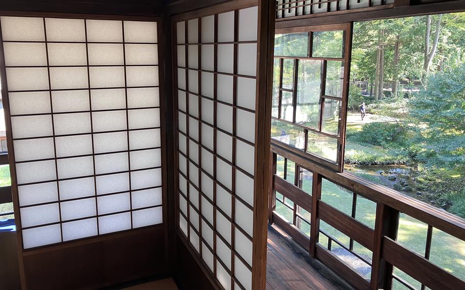 A wall of traditional Japanese wooden screens with paper panels and a window revealing a woodsy exterior.