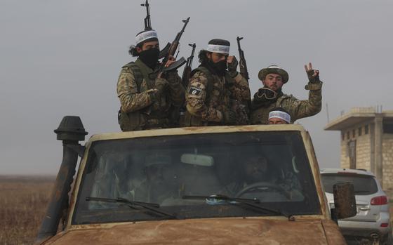 Men wearing combat gear and holding machine guns stand in the bed of a pickup truck.