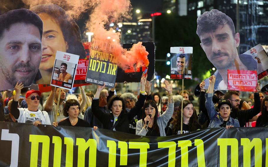 Demonstrators hold large cutouts of the faces of hostages held by Hamas and a large black banner.