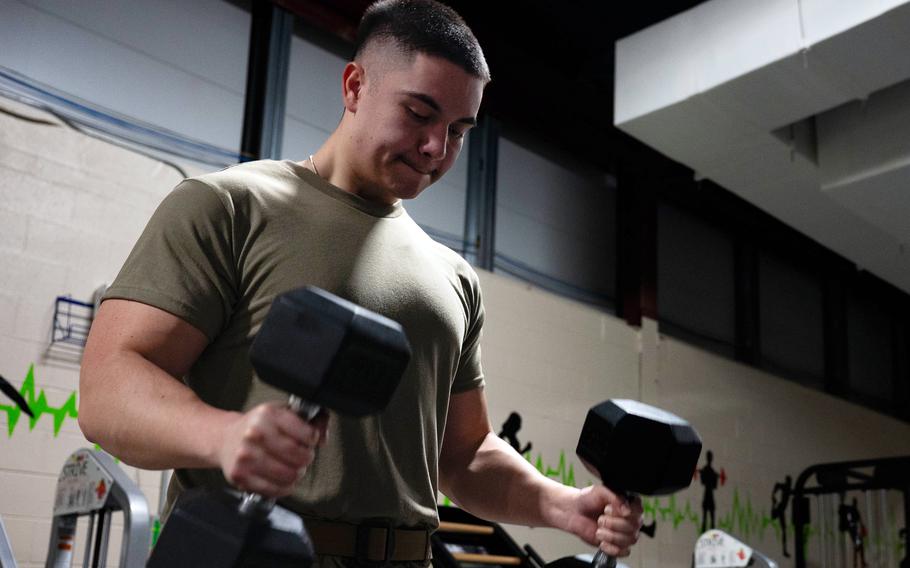 El soldado en pantalones de camuflaje y camisas de color verde oliva levanta pesas con sus propias manos mientras hace ejercicio en el gimnasio.